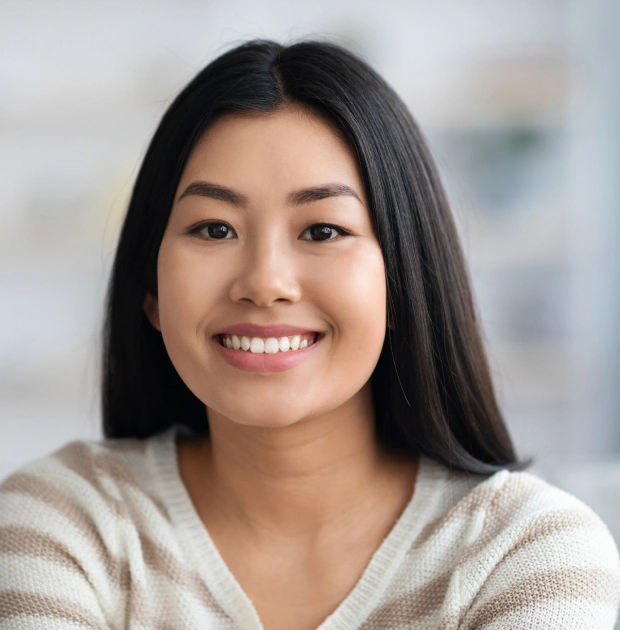 Smiling woman with long dark hair in casual beige sweater against blurred office background.