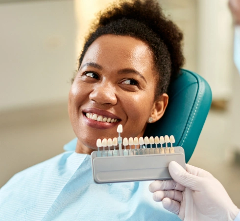 Smiling patient in dental chair with dentist holding teeth shade guide for color matching.