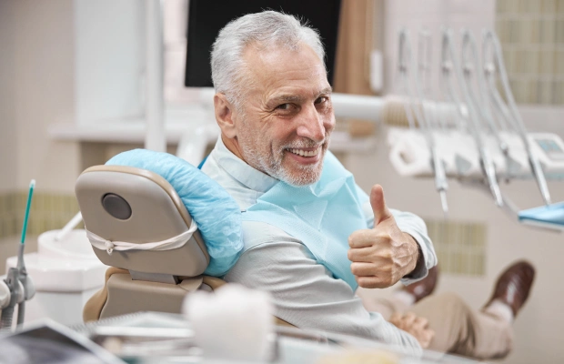 Senior man giving thumbs up in dental office chair with equipment visible
