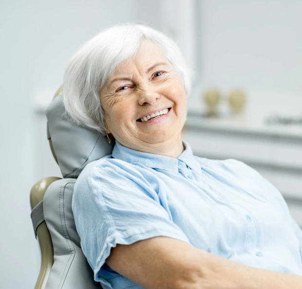 Smiling senior woman in dental chair wearing blue bib at SK2 Dental office