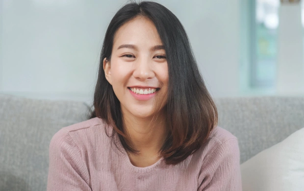 Smiling woman in pink shirt sitting on gray couch in dental office setting